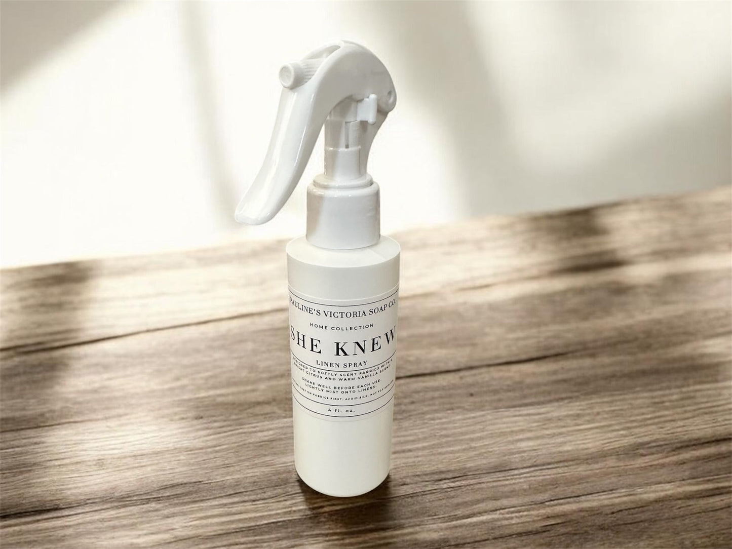 White spray bottle (linen spray) labeled 'She Knew' on a wooden surface with a blurred background