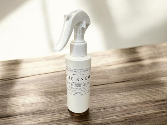 White spray bottle (linen spray) labeled 'She Knew' on a wooden surface with a blurred background