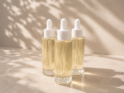 Three dropper bottles with a clear liquid on a beige surface with shadows.