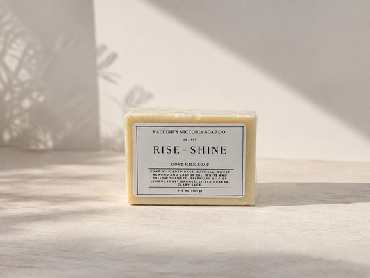 A rectangular bar of soap labeled 'Rise Shine' by Pauline's Victoria Soap Co., standing upright on a light surface with soft shadows cast across it.