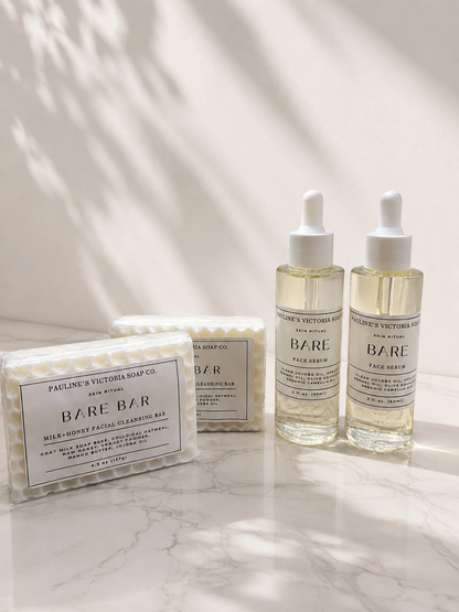 Bare skincare products including a bar soap and two serum bottles on a marble surface with soft lighting.