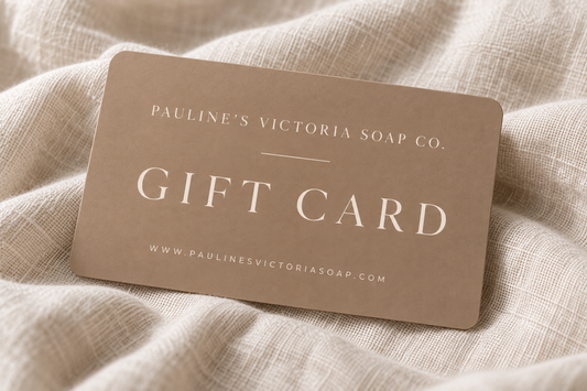 A rectangular gift card from Pauline's Victoria Soap Co. in a warm taupe-brown color, printed with white text, resting on a textured beige linen fabric background.