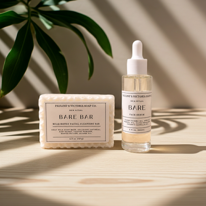 A skincare set from Pauline's Victoria Soap Co. featuring a rectangular Milk-Honey Facial Cleansing Bar and a clear dropper bottle of Bare Face Serum, styled on a light wood surface with leaf shadows.